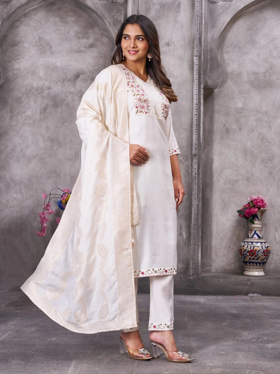 Woman in a white traditional outfit with embroidery standing against a gray textured wall.
